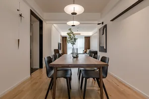 Modern dining room with wooden flooring, black chairs, and a long wooden table.