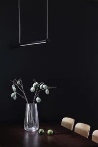 A modern interior setting featuring a glass vase with green fruits and oranges on a wooden tabletop.