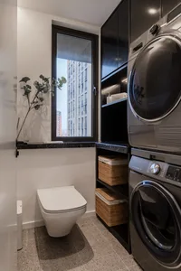 Modern laundry room with black cabinets, washing machine, dryer, and toilet, featuring a window with greenery.