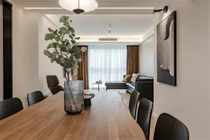A modern living room featuring a wooden table with a green plant in a clear vase, black chairs, a gray leather sofa, and a la