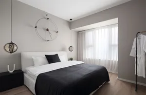A minimalist bedroom with a white bed featuring black bedding, white curtains, and a black and white hanging light fixture.