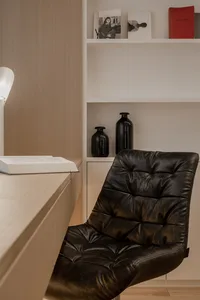 A modern minimalist home office with a black leather chair and a white bookshelf.