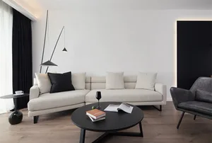 A minimalist living room featuring a white sectional sofa with black and white pillows, a black coffee table with a book and