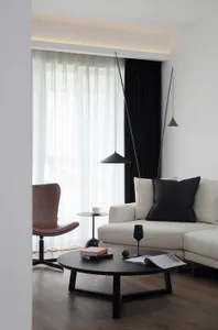 A minimalist living room featuring white furniture, a leather armchair, and a black coffee table.