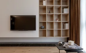 Modern minimalist living room with a flat-screen TV mounted on the wall, a wooden floor, and a black coffee table with books 