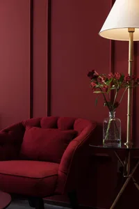 A cozy red upholstered armchair with a matching cushion, placed next to a glass side table holding a vase with red roses and