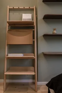A wooden bookshelf with shelves and a bag attached to it, featuring a book and a golden pineapple ornament.