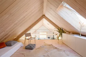 A minimalist attic bedroom with wooden floors, a bed, a chair, a cabinet, and a window providing natural light.