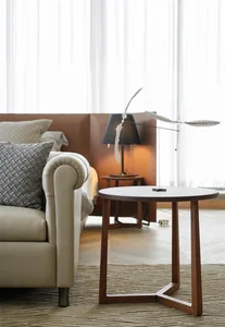 A minimalist bedroom featuring a leather sofa, fabric pillows, and a wooden side table.