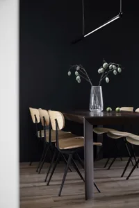 A minimalist dining room featuring wooden furniture and a dark wall.