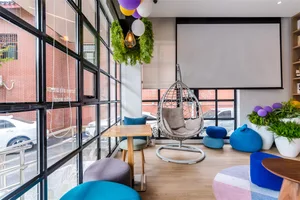 A modern cafe space with colorful furniture, large windows, and greenery.