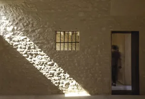 A modern interior design featuring a stone wall with light penetrating through a small window, creating dramatic shadows and 