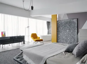 A modern minimalist bedroom featuring a bed with a gray blanket, leather headboard, and a yellow chair.