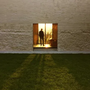 A man standing in a modern house with glass walls at sunset.
