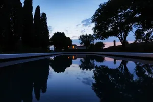 A serene evening view of a swimming pool reflecting the sky and surrounding trees.