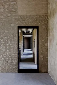 A modern corridor features concrete and brick walls with a stone accent, leading to a hallway with a wooden floor and a stone