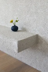 A minimalist concrete shelf featuring a black vase with a single flower arrangement.