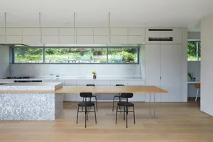 Modern kitchen with minimalist design, marble countertops, stainless steel appliances, and large windows overlooking greenery