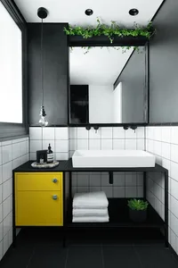 A modern bathroom with white tiled walls, black accents, a yellow cabinet, and a white sink.