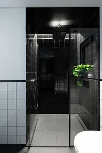 A sleek modern bathroom with black tiled walls and a glass shower enclosure, featuring a white toilet in the foreground and a