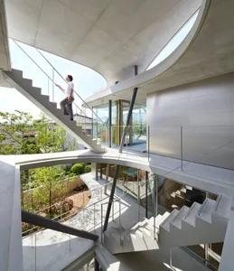 Person descending open staircase with curving concrete railings and glass balustrade, modern residential architecture, concre