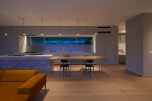 A modern kitchen and dining room with a marble island, wooden dining table, and concrete and glass finishes.