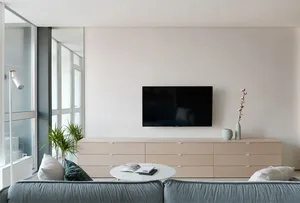 A modern living room featuring a wooden cabinet with a mounted television, a sofa, and decorative plants.