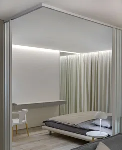 A minimalist bedroom with a bed, white curtains, and a small table lamp.