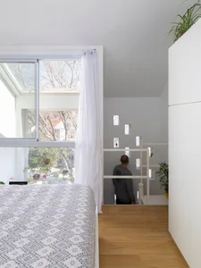 Minimalist bedroom with white walls, wooden floor, and large windows with sheer curtains.