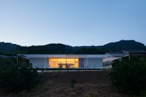 Modern minimalist concrete house at dusk with illuminated interior.