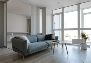 A modern minimalist living room featuring a light-colored wooden floor and a sleek, contemporary sofa with glass elements.