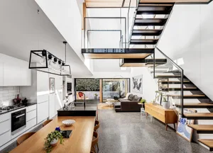 Modern living room and kitchen with an open-concept floor plan, featuring a glass staircase and concrete flooring.