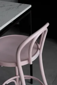 A modern interior featuring a pink plastic chair next to a marble table with black legs.