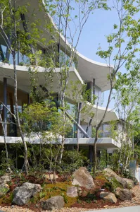 一座現代住宅建築，外牆採用混凝土與玻璃材質，周圍環繞綠意與岩石。