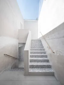 Close-up view of a modern indoor staircase with concrete steps and white walls, featuring a single brass handrail.