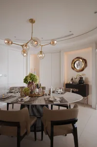 Modern dining room featuring a circular marble table, upholstered beige chairs, and a stylish brass chandelier with multiple 