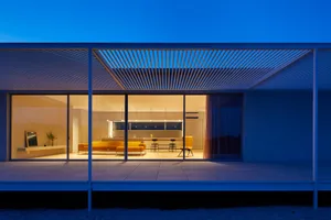 A modern house exterior with a glass roof at dusk.