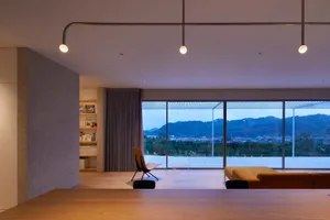 Modern living room with large windows offering a view of mountains and buildings at dusk.