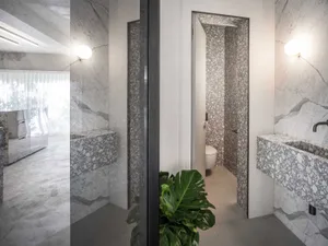 Modern bathroom with marble walls and floor, featuring a sleek white toilet and a green plant.