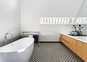 A modern minimalist bathroom featuring a white bathtub, black and white geometric tiles, and wooden vanity.