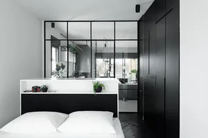 A minimalist bedroom features a sleek, black-and-white color palette, with a glass partition, wooden flooring, and metal fixt