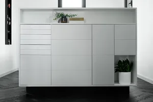A modern, minimalist white concrete storage unit with three drawers, four doors, and open shelving.