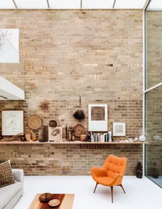 A modern living room featuring a brick wall, an orange armchair, a wooden coffee table, and various decorative items on a low