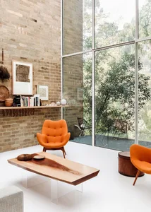 A modern living room featuring wooden furniture, orange accent chairs, and large windows.