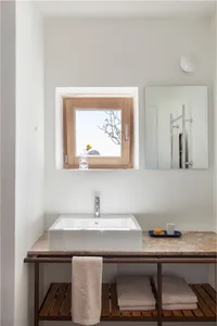 A minimalist bathroom features a white concrete sink, a marble countertop, and a metal faucet, with a small window and a mirr