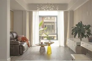 Minimalist living room with a brown leather couch, glass side tables, and potted plants.