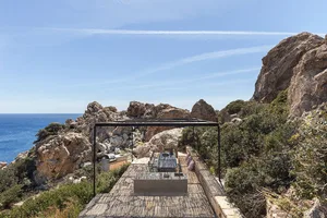 A minimalist outdoor seating area with a table and chairs on a wooden deck overlooking the sea.