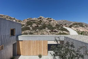 A modern building with concrete exterior and minimalist design, featuring a rocky hill in the background.
