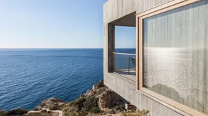 A modern house with a concrete exterior and large window overlooking the ocean.