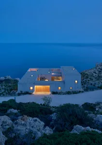 Modern house with concrete exterior located near a rocky coastline.